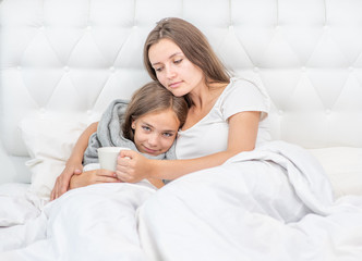 Mom taking care of sick daughter in bedroom and giving her cup of tea
