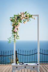 Wedding arch decorated with white and pink roses and green leaves. Outdoor wedding ceremony. Sea background