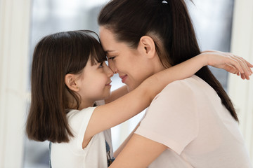 Cute little daughter touching foreheads with mother.