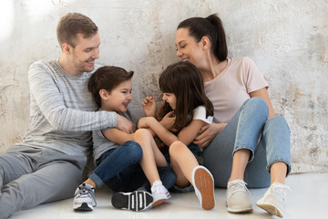 Happy young parents with little kids sitting on floor.