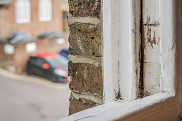 Close-up, shallow focus of a wooden styled, sash window seen in the opened position. Signs of rot can be seen on the wood. In the distance is part of a carpark used for this London office block.