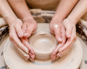 loving couple in the studio make clay dishes together on a potter’s wheel