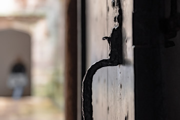 Shallow focus of a medieval wooden door and iron latch in a popular tourist site. A visitor can be seen entering a distant archway.