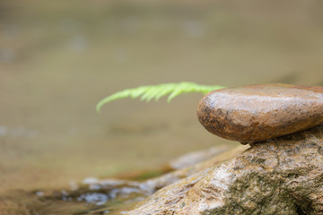 Background concept. A stacked stone with leaves on top and a waterfall background.