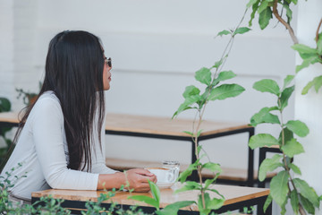 A beautiful woman wearing a long-sleeved white shirt sitting at a coffee shop.