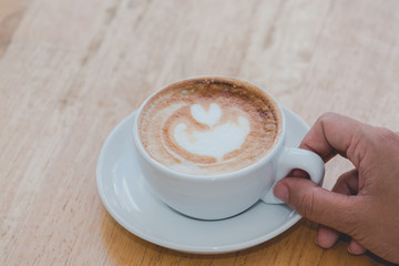 The coffee cup is placed on a wooden floor and the woman's hand is held on the ear.