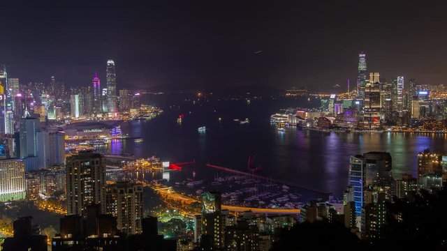 Timelapse various Hong Kong motorboats sail on wide harbor reflecting city highrise buildings and towers silhouettes at night zoom out