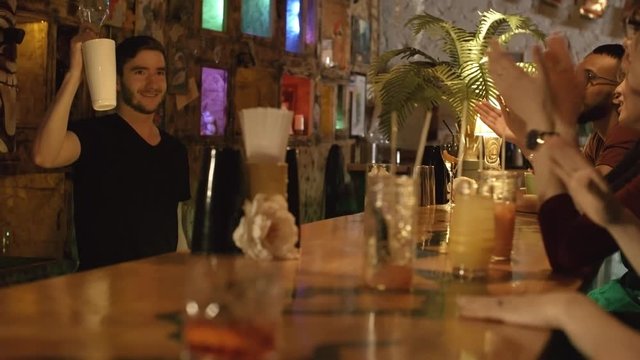Skilful young bartender entertaining guests and smiling when making cocktails for them, they clapping hands