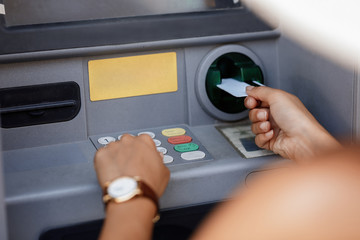 Close-up of woman entering pin while using ATM machine.