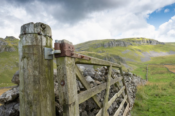 Close-up, shallow focus of an damaged and abandoned fence seen broken to one side. A rock wall is...