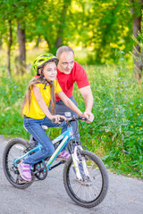 happy young father teaches his daughter to ride a bicycle in the summer park