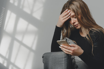 Portrait of a young sad crying girl with a smartphone in her hand.