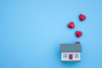 A small house, three hearts fly out of the pipe on a blue background. The concept of buying, selling, renting real estate, mortgages, happiness in your homeю Place for text
