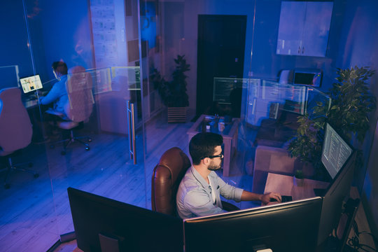 Profile photo of it specialist guy sitting chair work late at night seriously looking monitors writing secure code for website server content development expert night office indoors