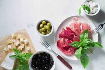 Set of jamon Iberico and Serrano on a white plate with olives, cheese and basil. Antipasti snack