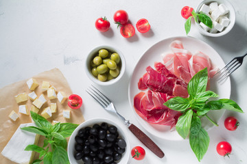 Set of jamon Iberico and Serrano on a white plate with olives, cheese and basil. Antipasti snack