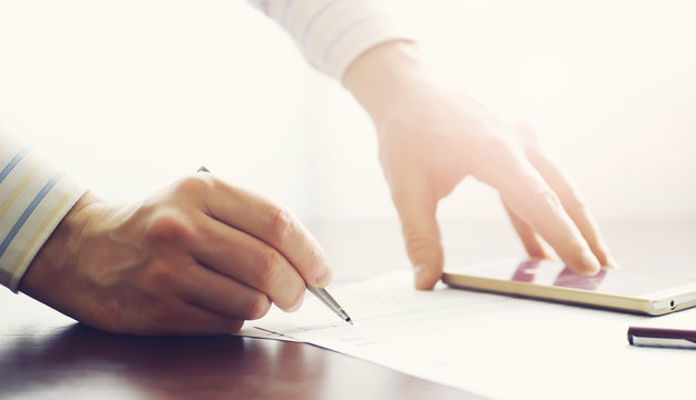 Business meeting. A man signs a contract. Male hand with pen makes notes in the office.