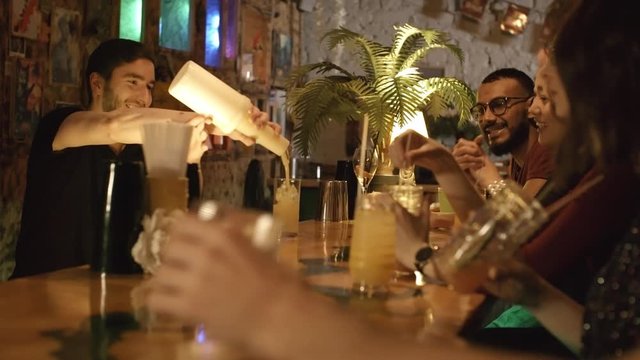 Young bartender pouring drinks into glasses when making cocktails for customers, they clapping hands