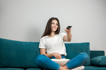 beautiful young woman changes channel while watching TV and eating popcorn feeling comfortable on the sofa at home