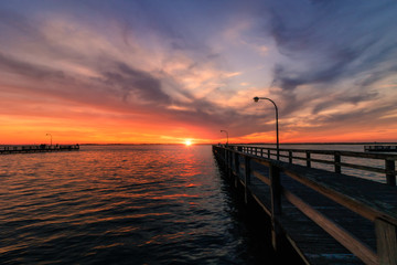 Fototapeta na wymiar Beautiful vibrant colors in the sky over a long fishing pier as the sun dips below the horizon at sunset. 