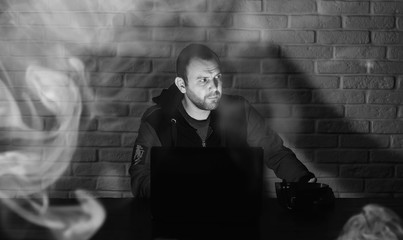 Fototapeta premium Hacker in black mask and hood at the table