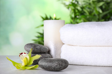 Exotic flower, spa stones, candle and towels on grey table against blurred green background, space for text