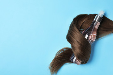 Spray bottle wrapped in lock of hair on light blue background, flat lay with space for text. Natural cosmetic products