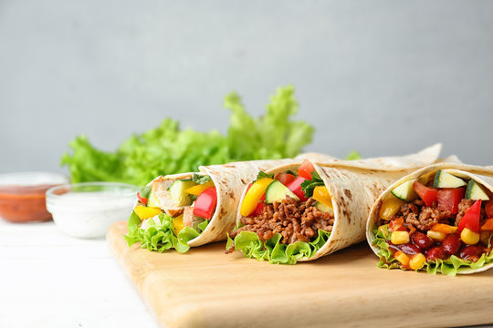 Delicious meat tortilla wraps on white wooden table against grey background
