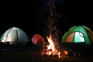 Bonfire near camping tents outdoors at night