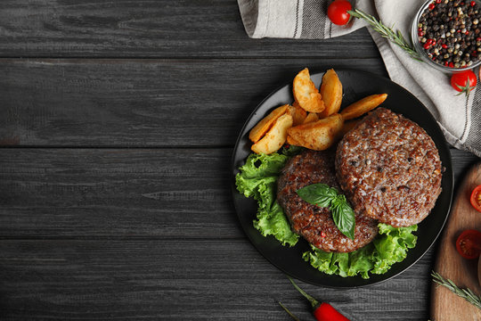 Flat lay composition with grilled meat cutlets for burger on black wooden table. Space for text