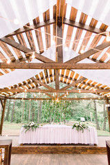 Rustic tent restaurant with wedding or dinner table and floral decorations and light bulbs, on a...