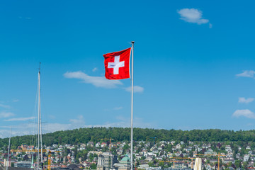 National flag of Switzerland flying at the Zurich lake against blue sky