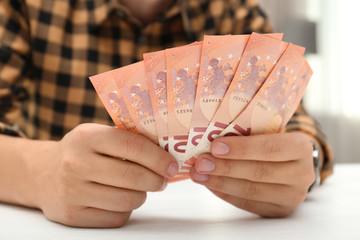 Man with Euro banknotes at table indoors, closeup