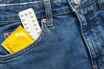 Closeup view of jeans with yellow condom and birth control pills in pocket. Safe sex concept