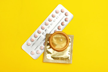 Condoms and birth control pills on yellow background, flat lay. Safe sex concept
