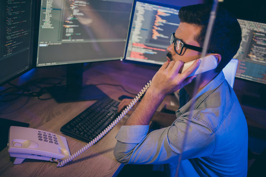 Profile photo of it-specialist guy work late at night sitting office chair looking monitors speaking phone website debugging expert correct service error office indoors