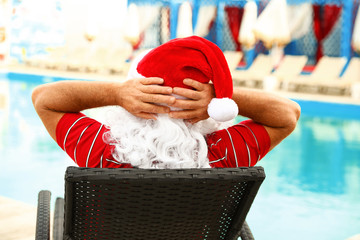 Obraz premium Authentic Santa Claus resting on lounge chair near pool at resort, back view