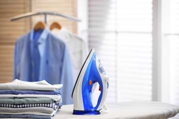 Board with modern iron and stack of clothes indoors, space for text. Laundry day