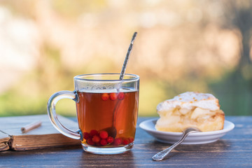 Tea glass with sweet cake and book on wooden table in the morning, outdoors