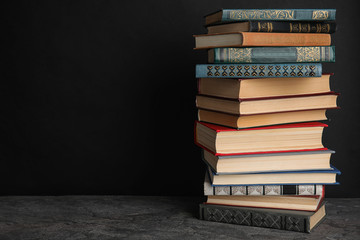 Stack of hardcover books on grey stone table against black background. Space for text