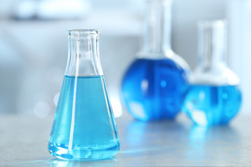 Conical flask with light blue liquid on table in laboratory. Space for text