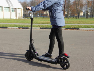 Obraz premium Dziewczyna w jesiennym ubraniu przyjeżdża z przenośną elektryczną hulajnogą na Park w słoneczny dzień, ekologiczny transport miejski