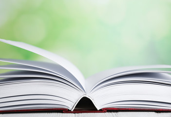 Open book on white wooden table against blurred green background, closeup. Space for text
