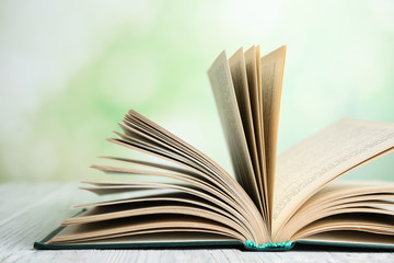 Open book on white wooden table against blurred green background, closeup