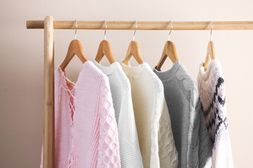 Collection of warm sweaters hanging on rack near light wall