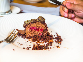 Eating delicious chocolate cake with fresh berry jam, ganache mousse cake with raspberry sauce, gold decoration Dessert