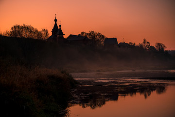 Panorama of the pink sunrise on the misty river with silhouette of the old church