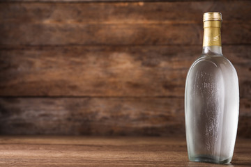 Bottle of vodka on table against wooden background. Space for text
