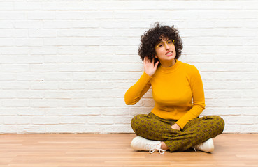 young pretty afro woman looking serious and curious, listening, trying to hear a secret...