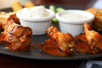 Buffalo wings with sauce, celery, carrots on a black plate. Bokeh effect.